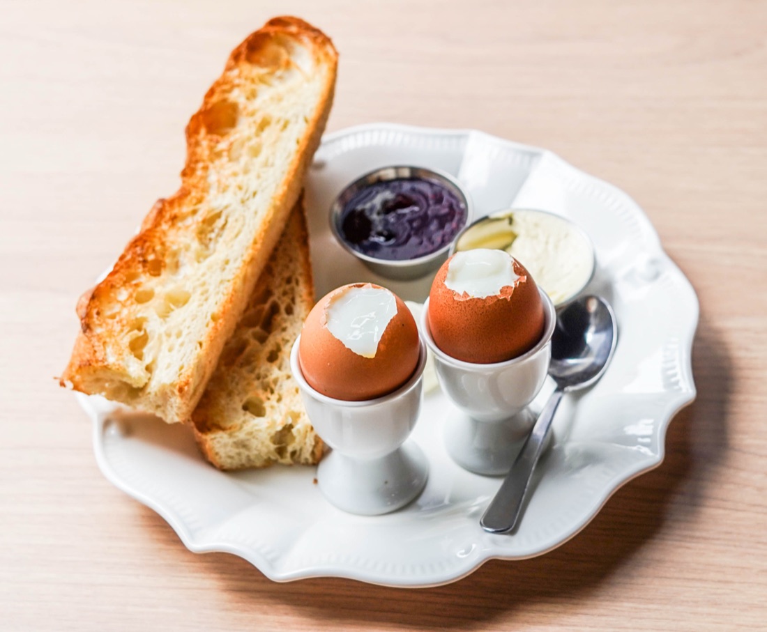 Breakfast plate with soft-boiled eggs, berries compote and focaccia